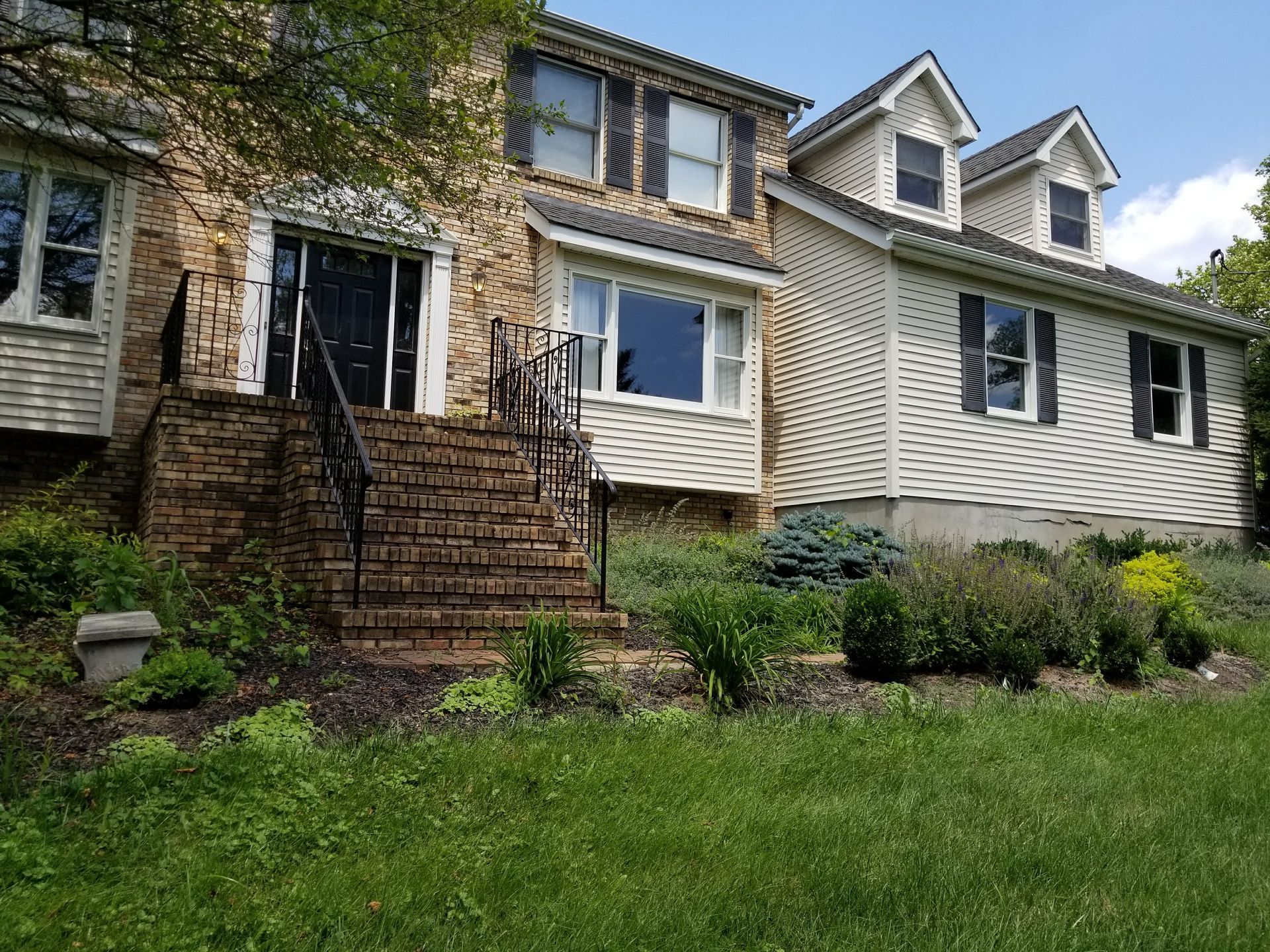 Stone house with white siding, front steps, and green lawn on a sunny day