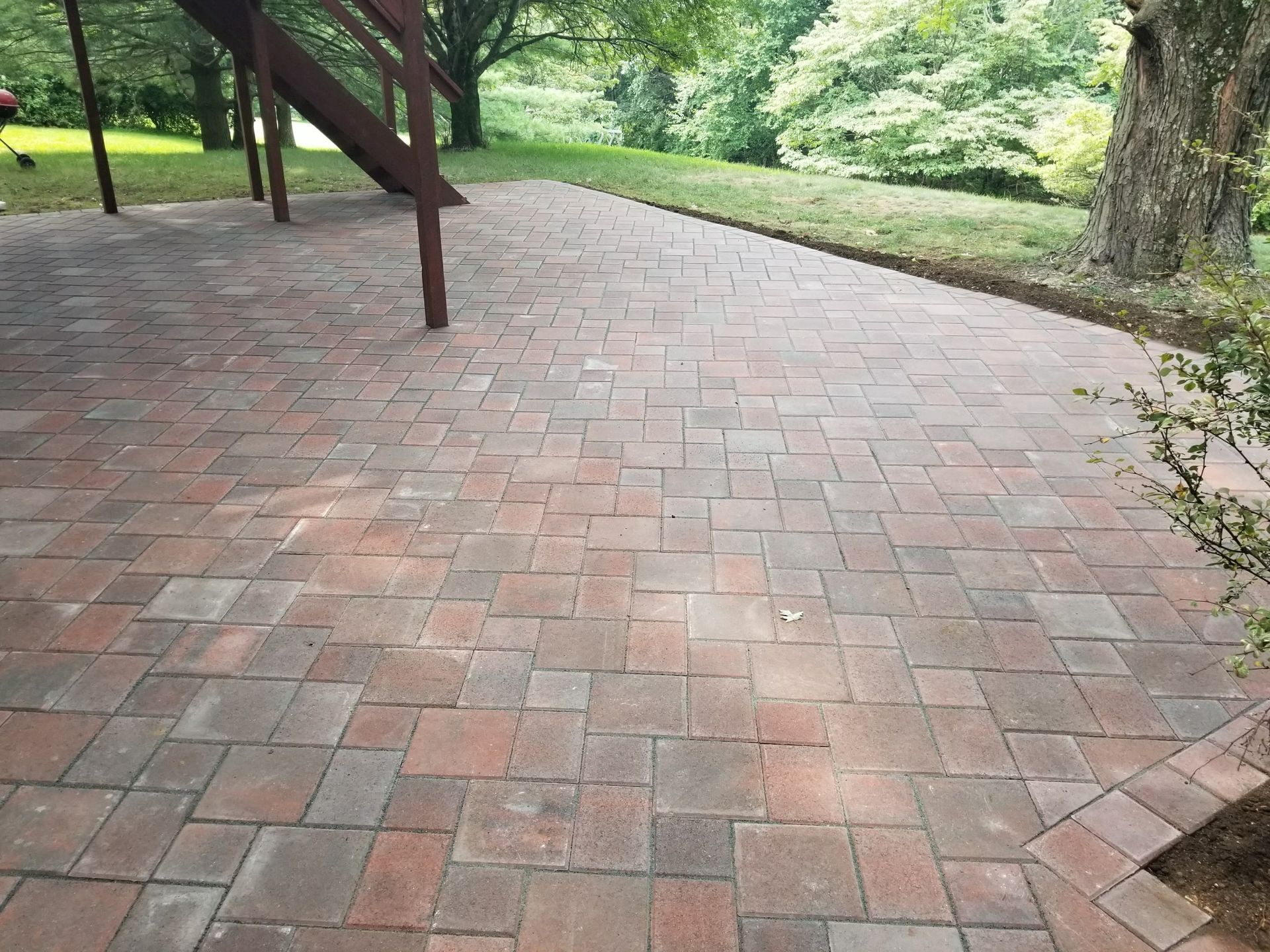 Brick patio beside green trees and a wooden deck in a park-like yard