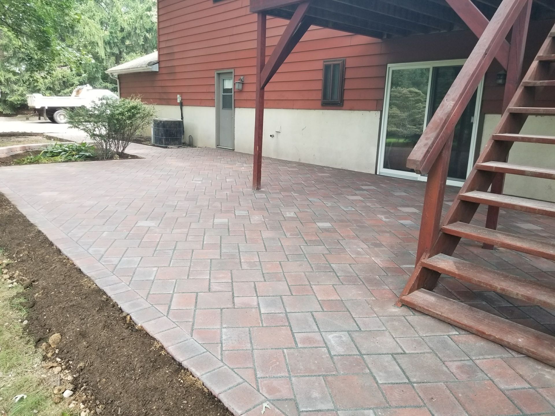 Brick patio beside a red house with white foundation and exterior wooden stairs