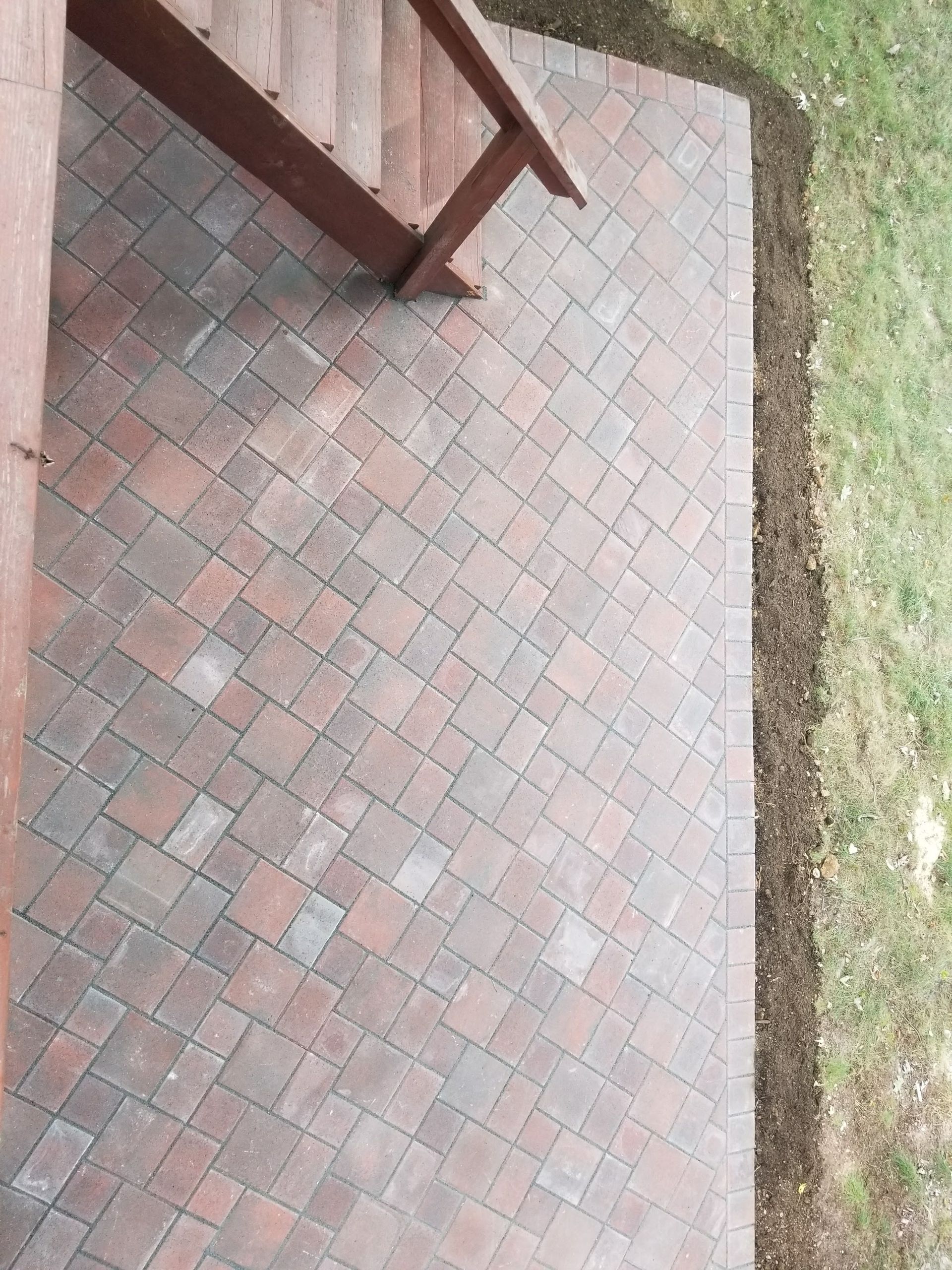 Brick patio beside a grassy lawn, with part of a wooden bench at the top left.