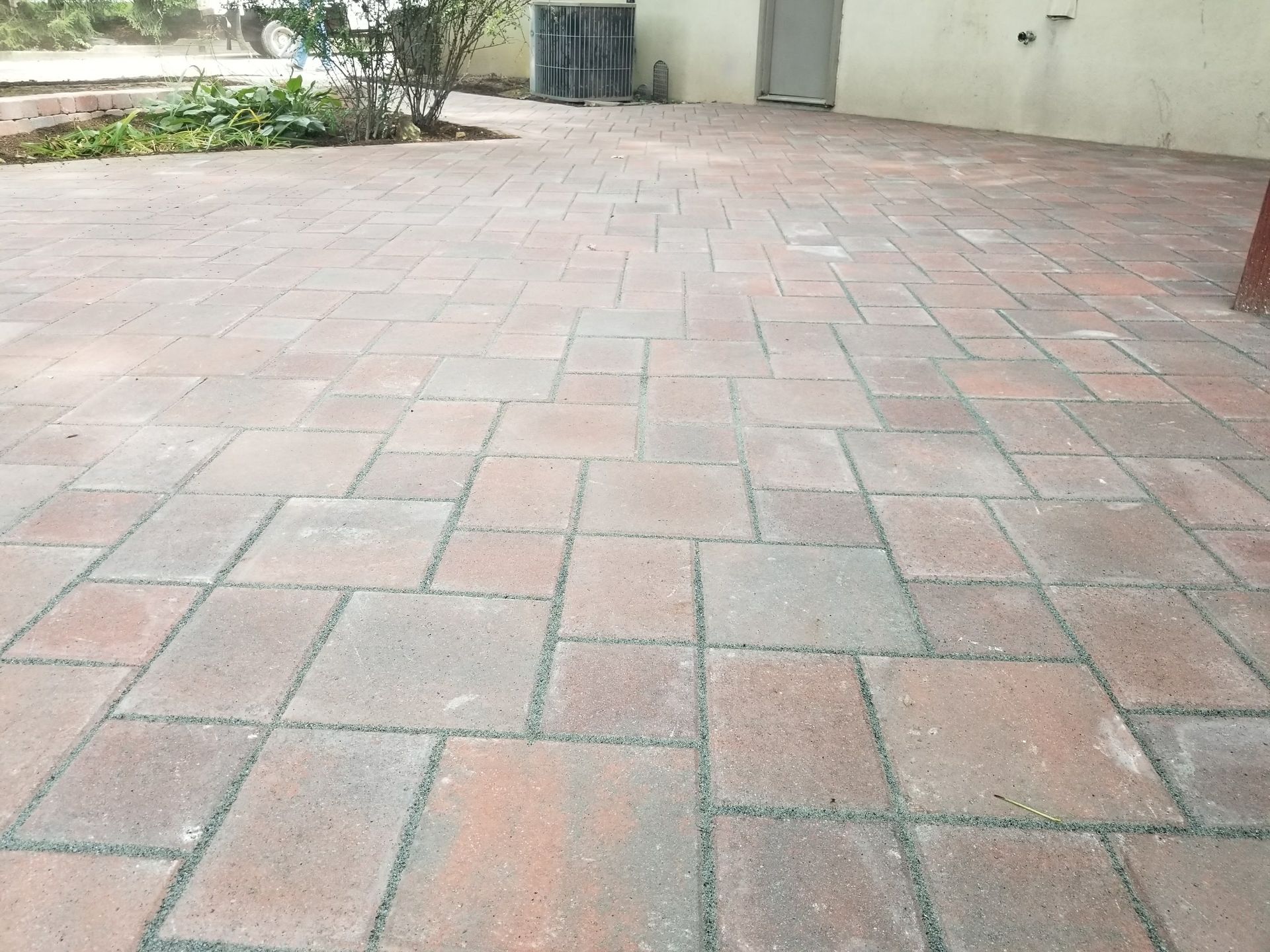 Empty brick-paved courtyard beside a light-colored building and a few trees