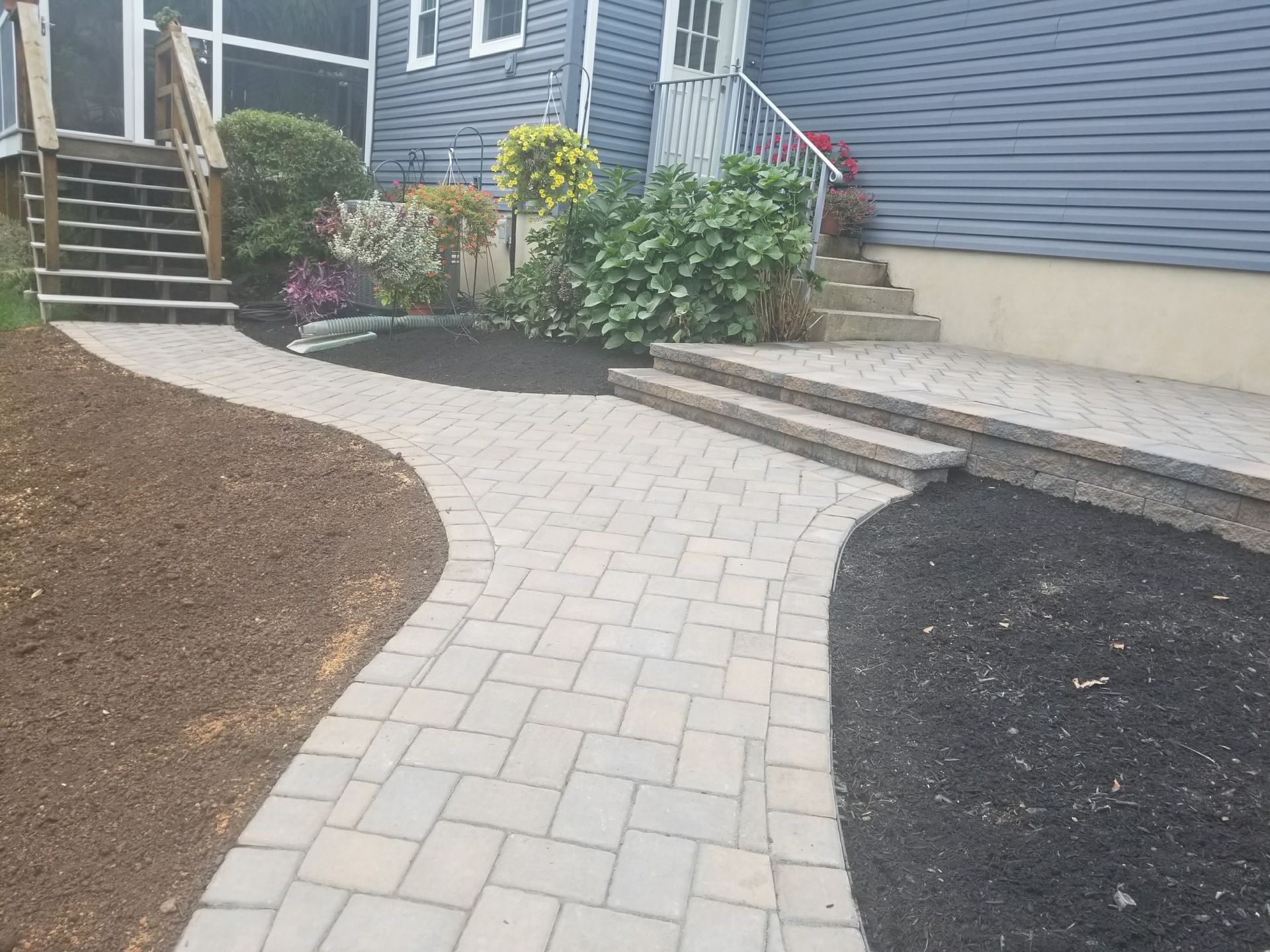 Curved paver walkway leading to house steps, bordered by mulch beds and shrubs.