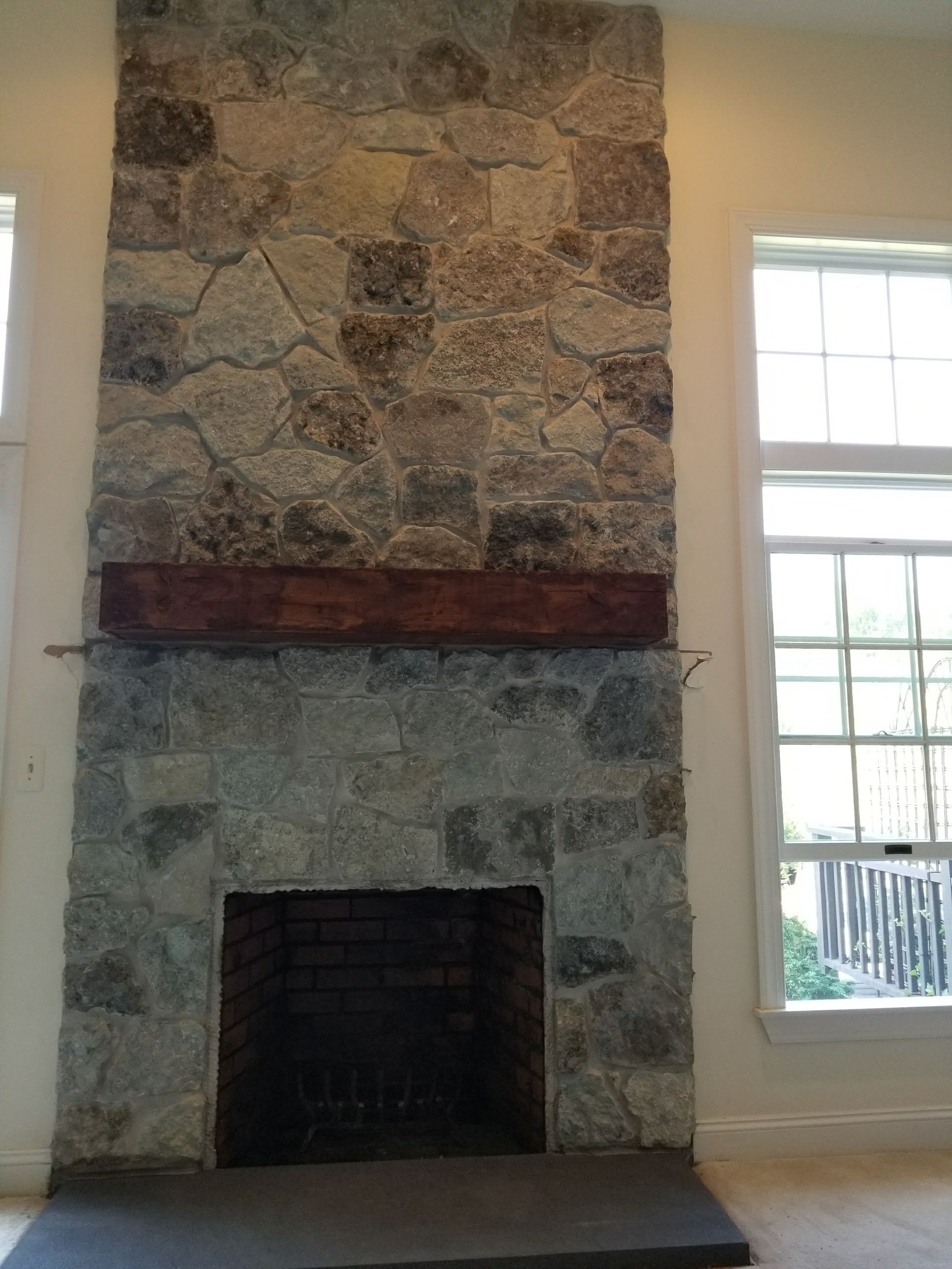Stone fireplace with a dark firebox and a wooden mantel beside a window in a bright room