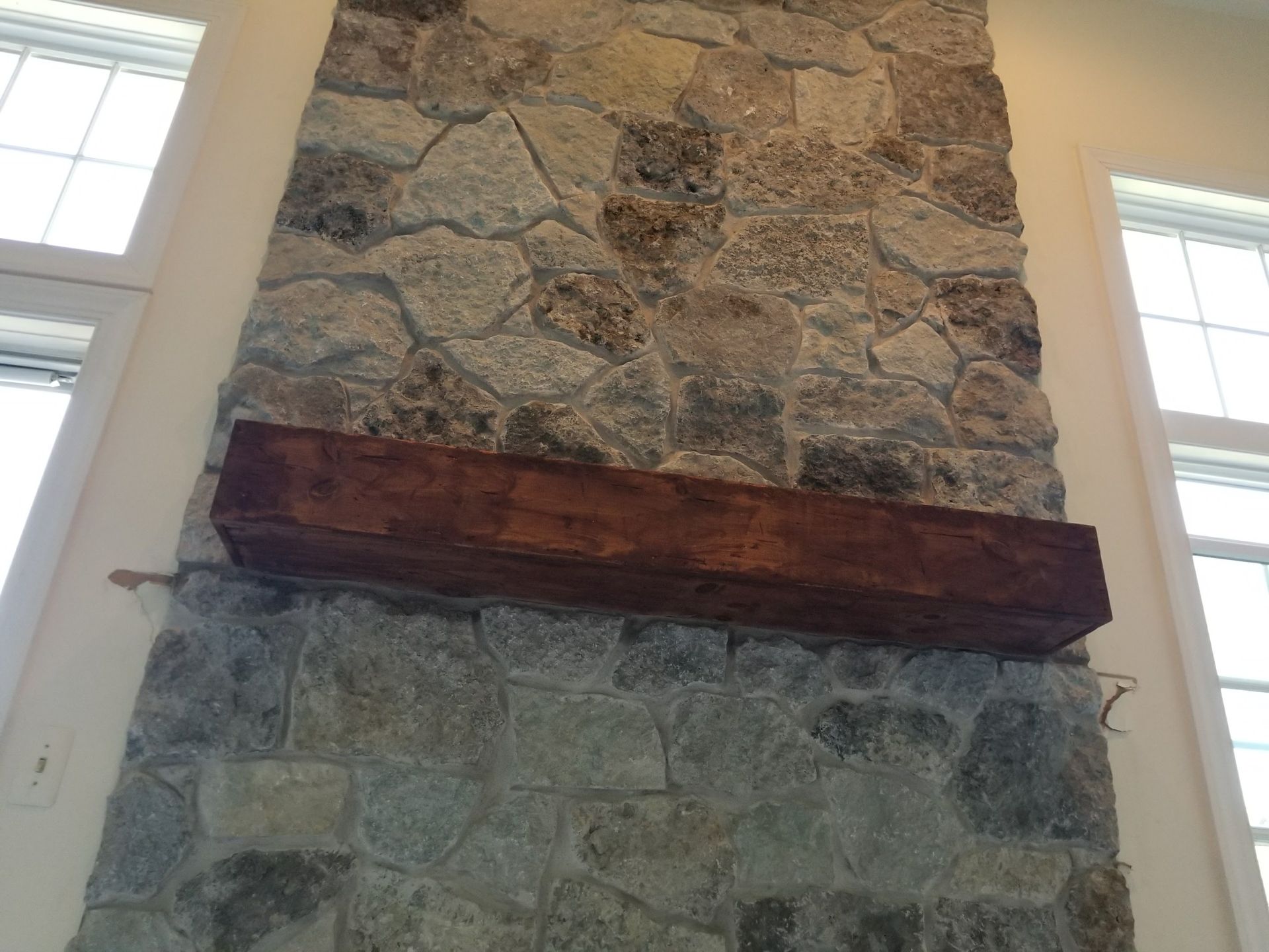 Stone fireplace with a dark wooden mantel between two tall windows