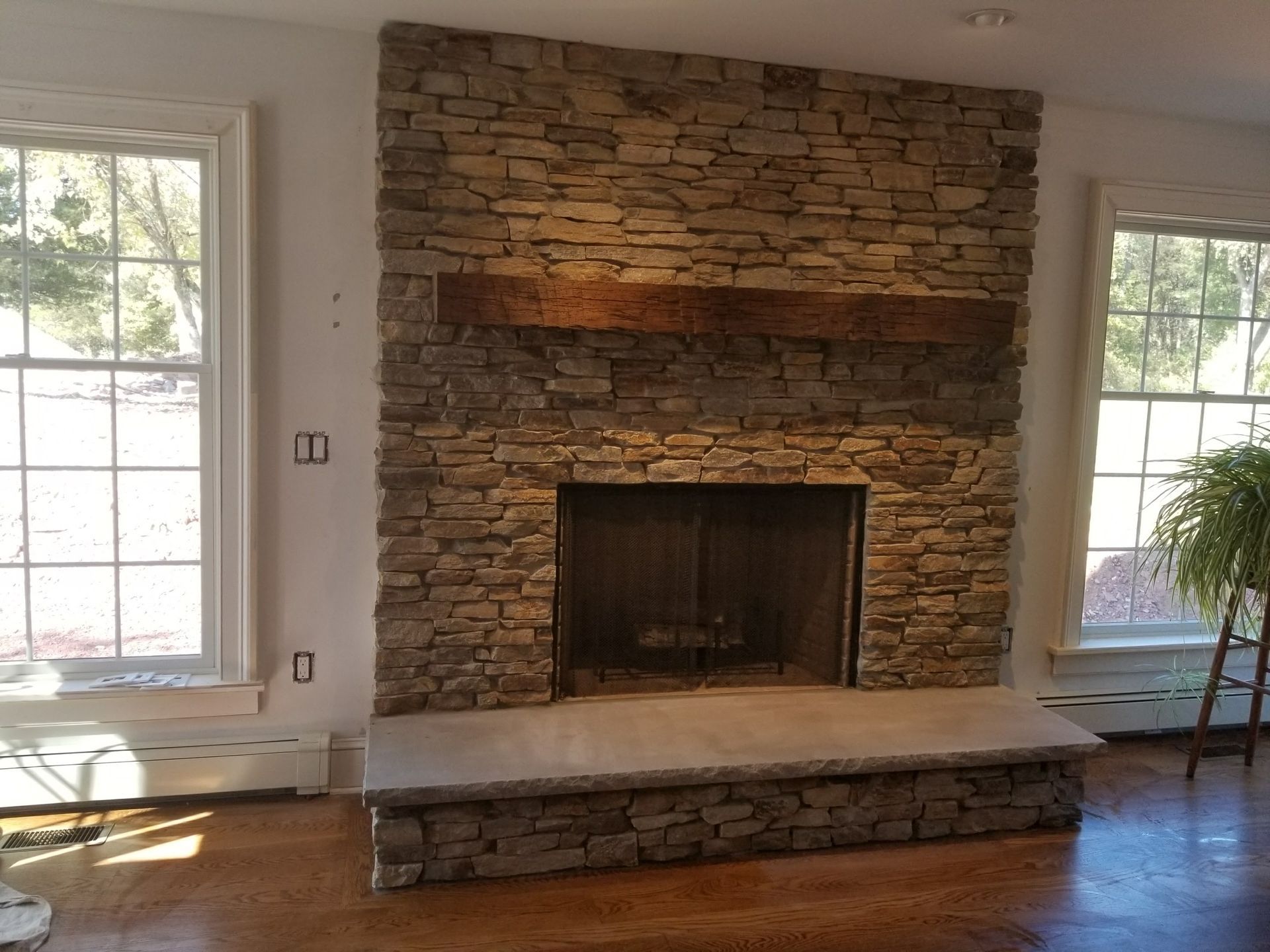 Stone fireplace with raised hearth centered between two large windows in a bright living room