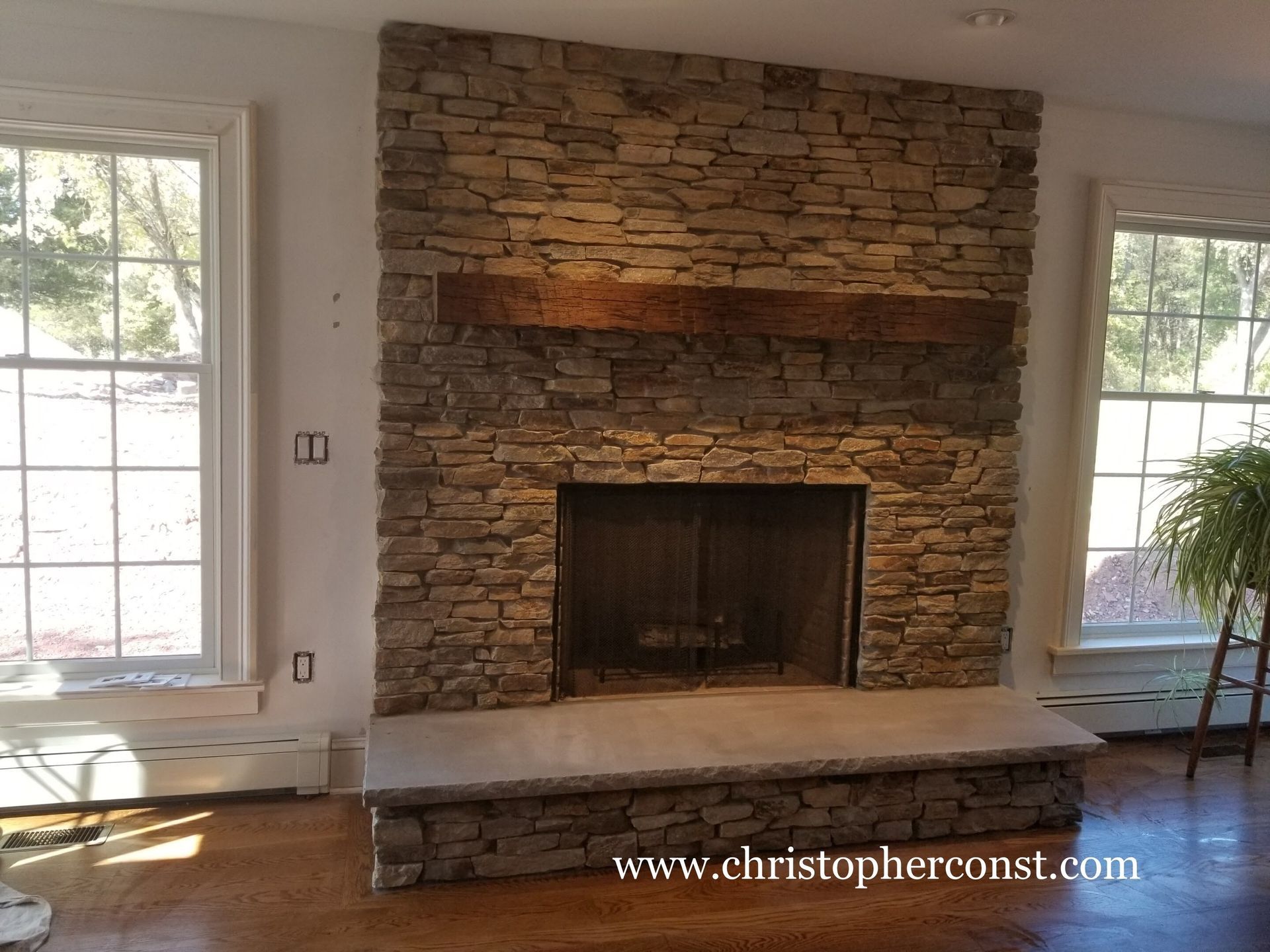 Stone fireplace with raised hearth in a bright room, flanked by two windows.