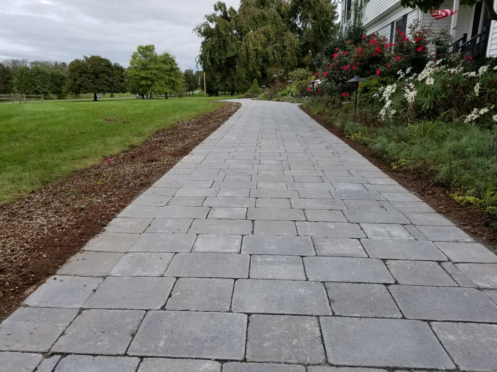 Stone walkway leading through a green garden beside a house and flower bed