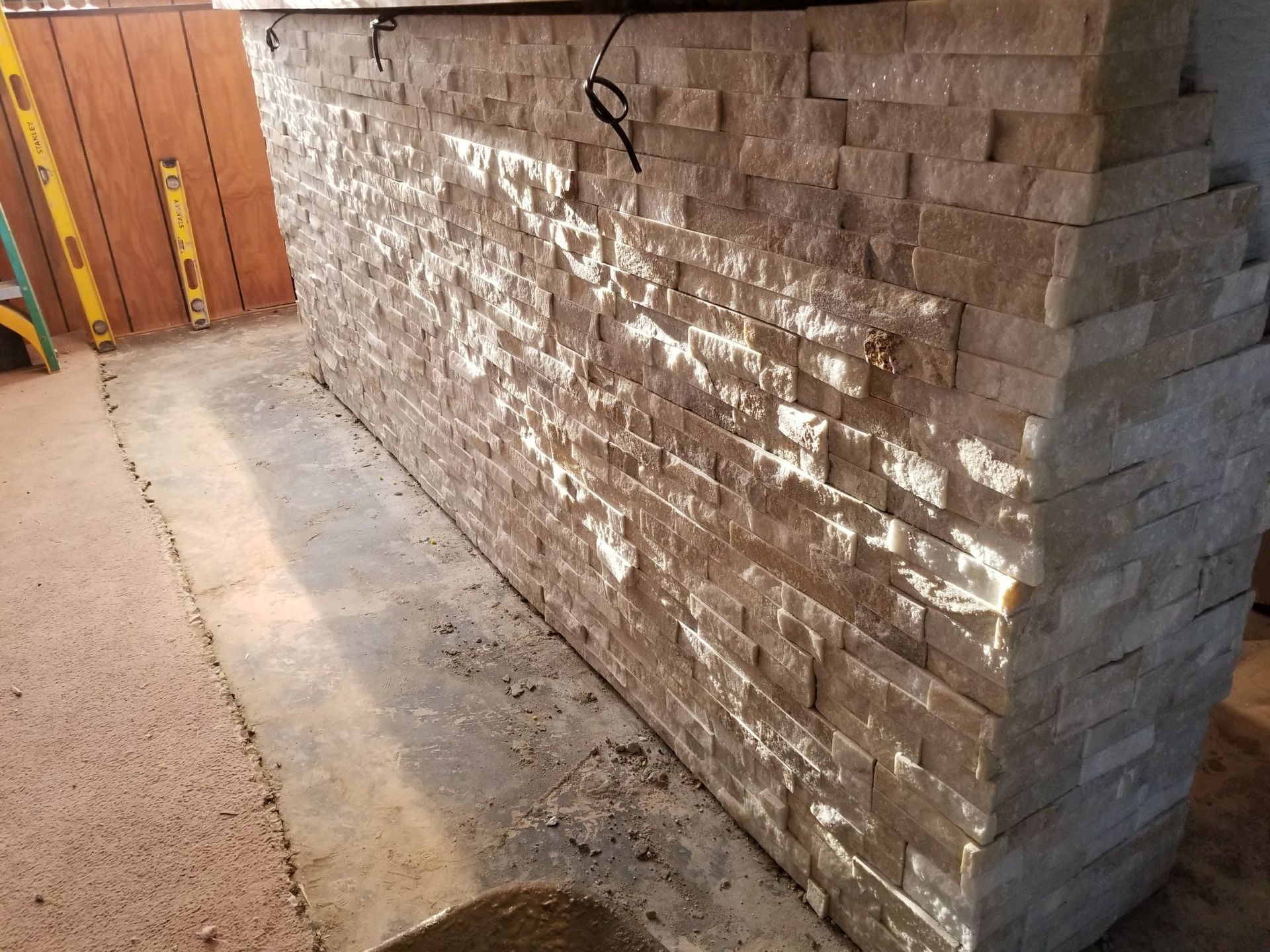 Stone veneer wall in a hallway, with bright reflected light and a concrete floor.