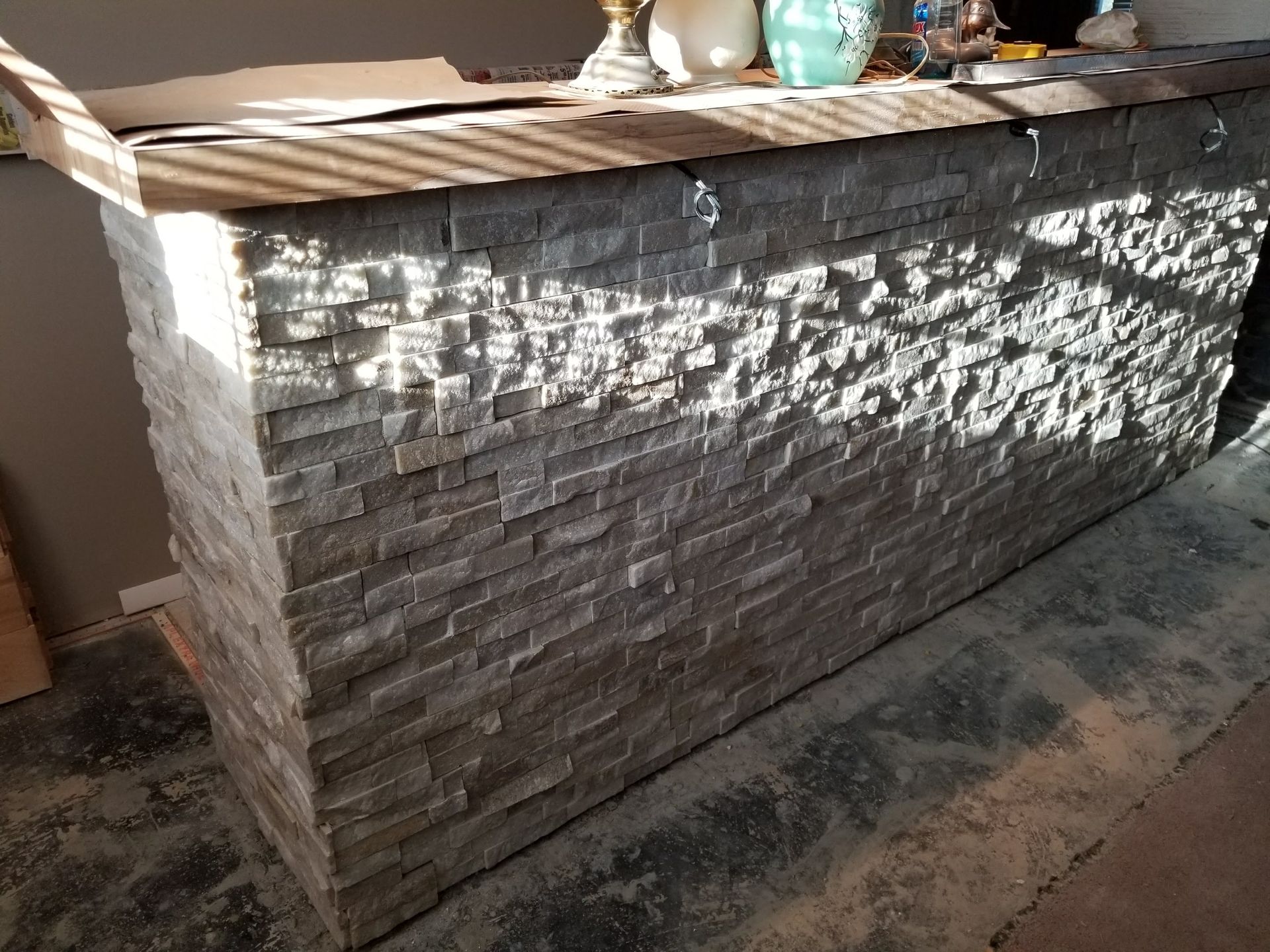 Stone-faced bar counter in sunlight, with a wooden top and tiled floor beside it.