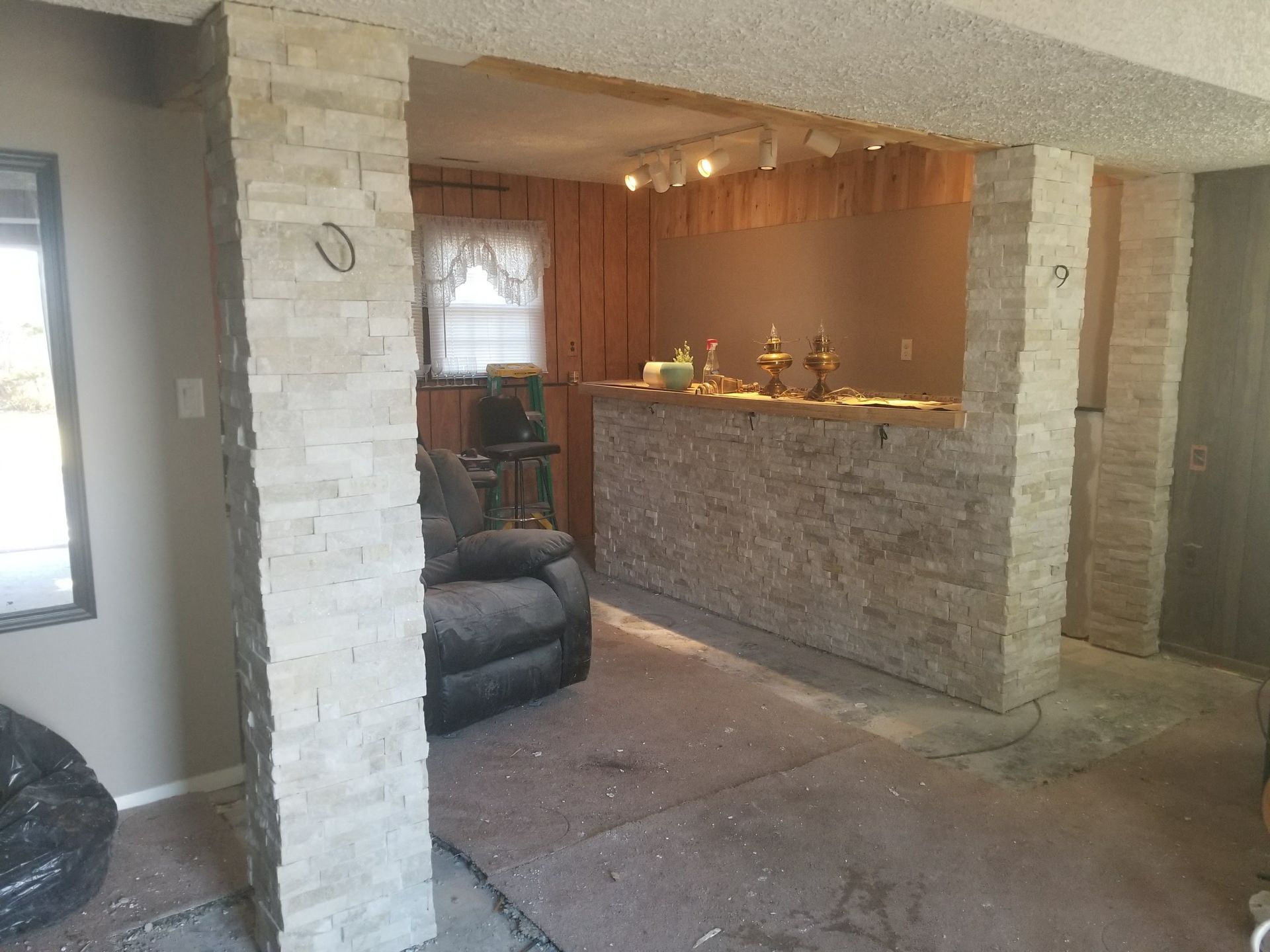 Stone basement living room with exposed beams, bar counter, recliner, and carpeted floor