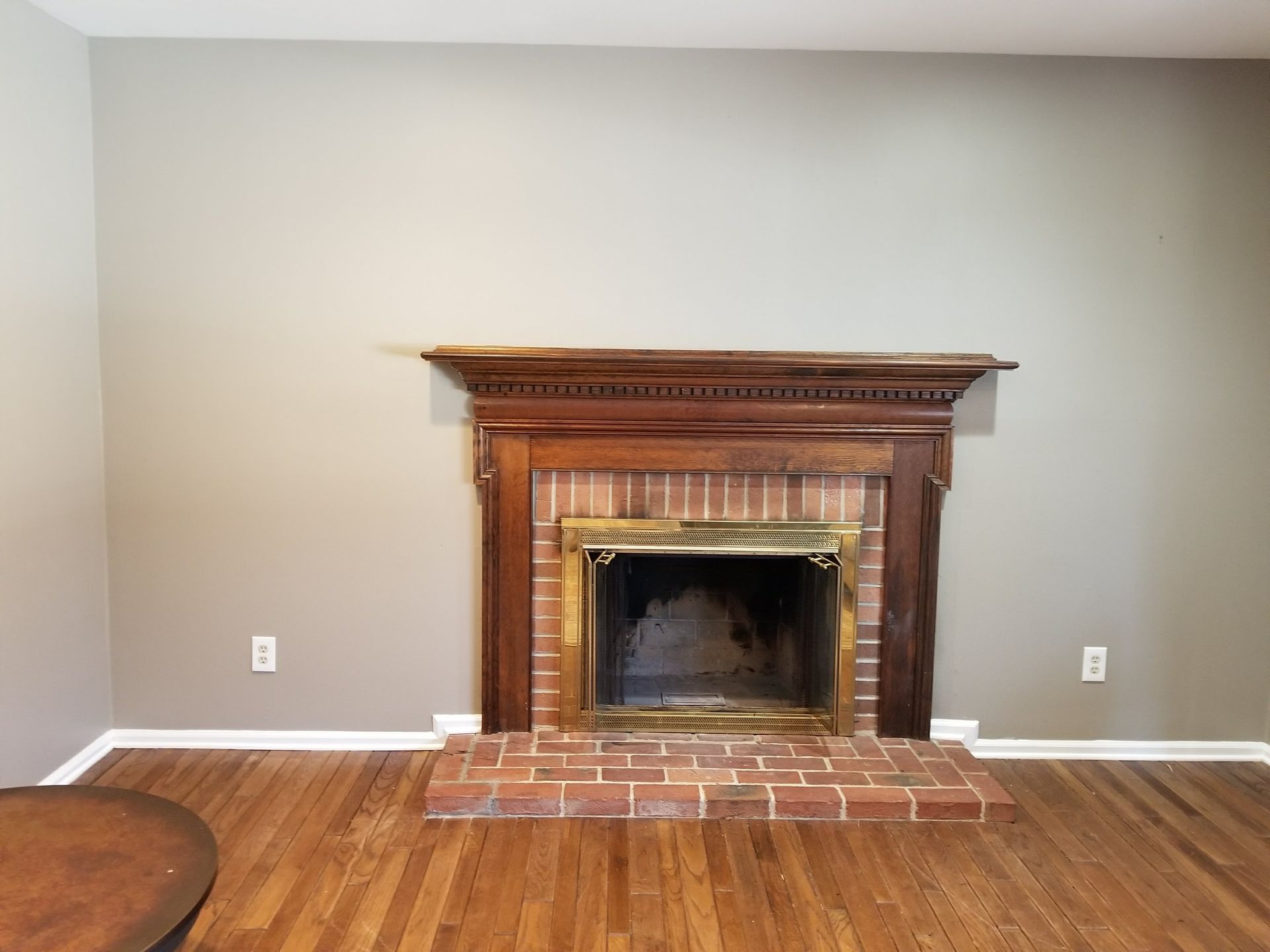 Empty room with a wooden fireplace mantel and brick hearth on a gray wall