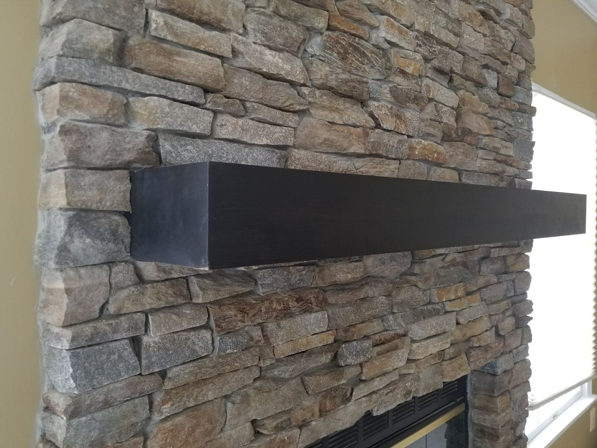 Stone fireplace with a black metal mantel shelf extending from the wall