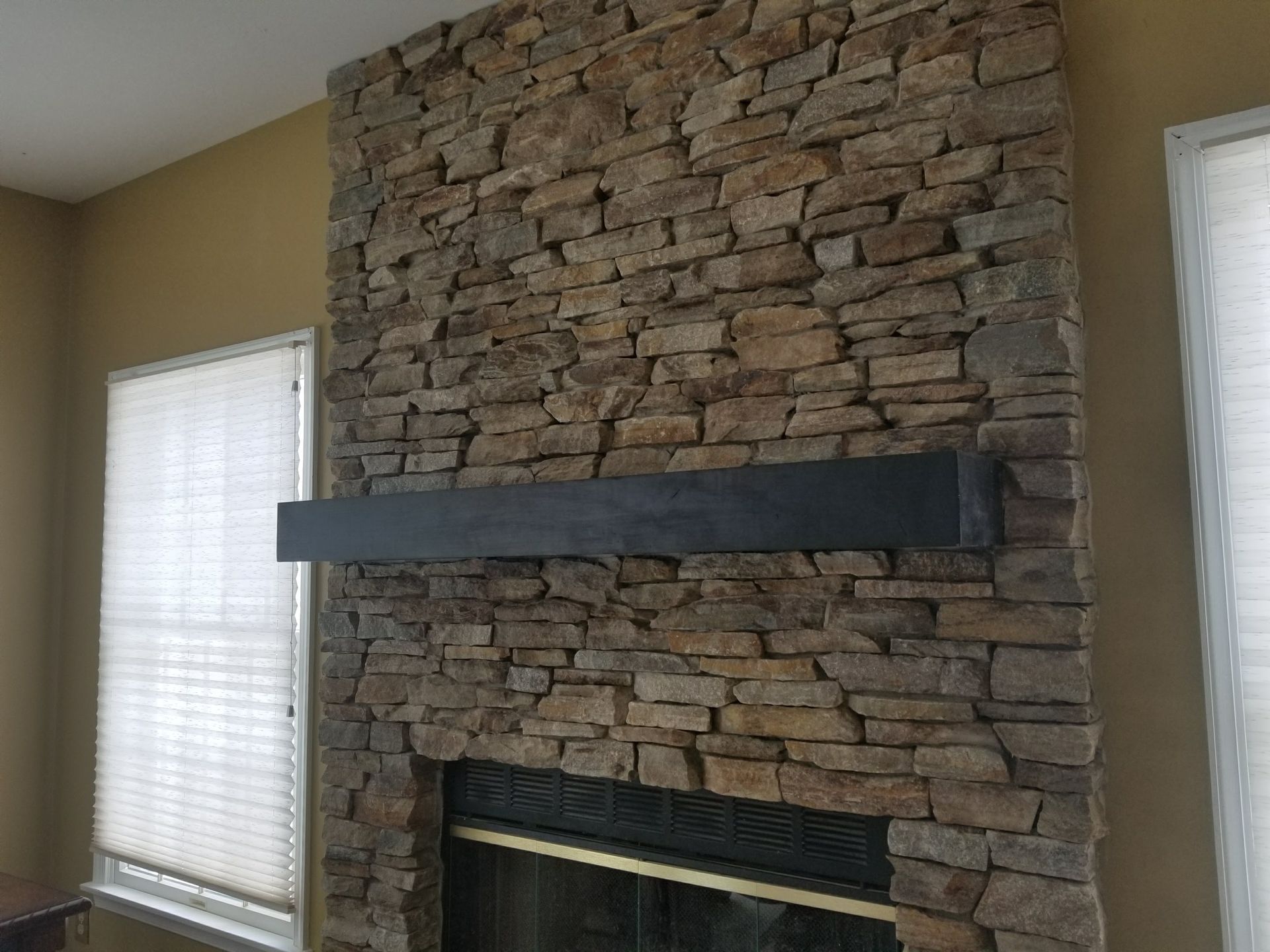 Stone fireplace wall with a dark mantel and two windows on either side