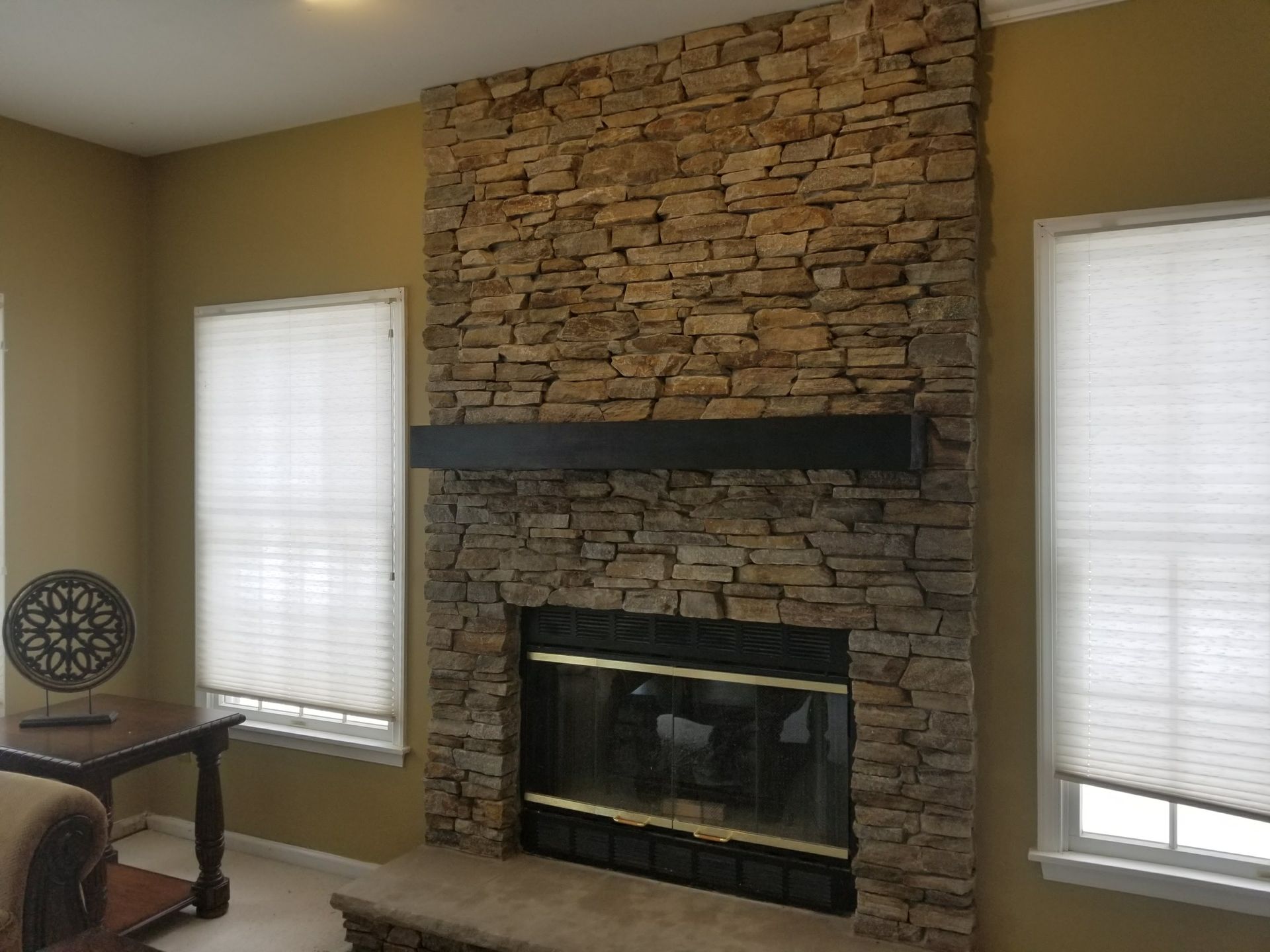 Living room with stone fireplace, dark mantel, and two windows with blinds