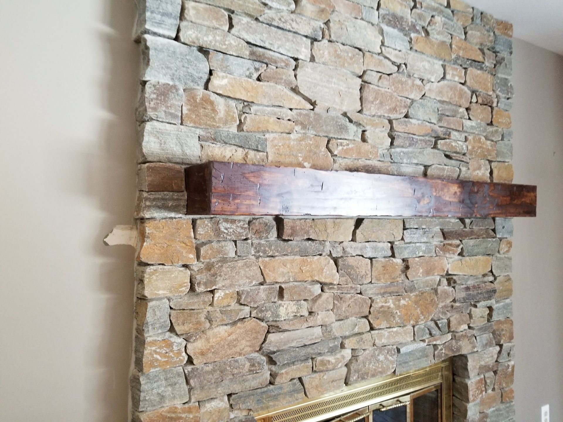 Stone fireplace surround with a dark wooden mantel shelf in a beige room