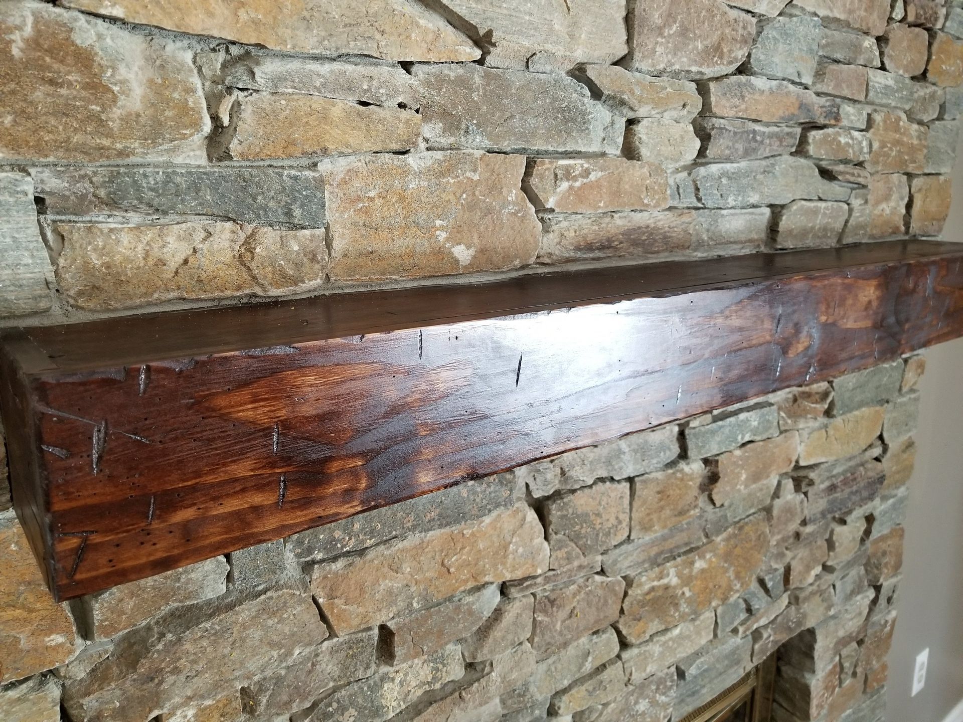 Dark wooden mantel shelf mounted on a stone wall