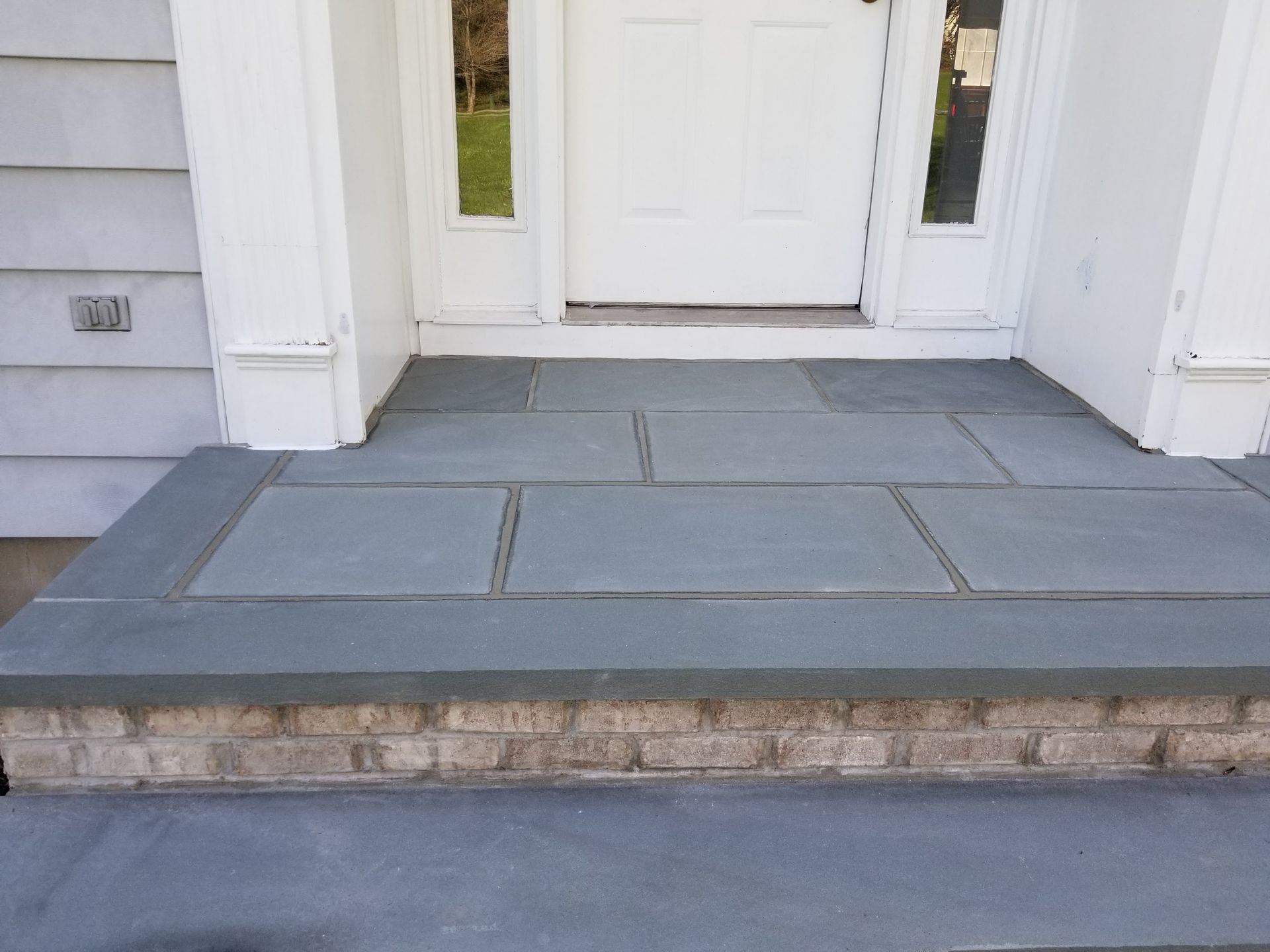 Front porch with gray tiled steps leading to a white front door and siding.