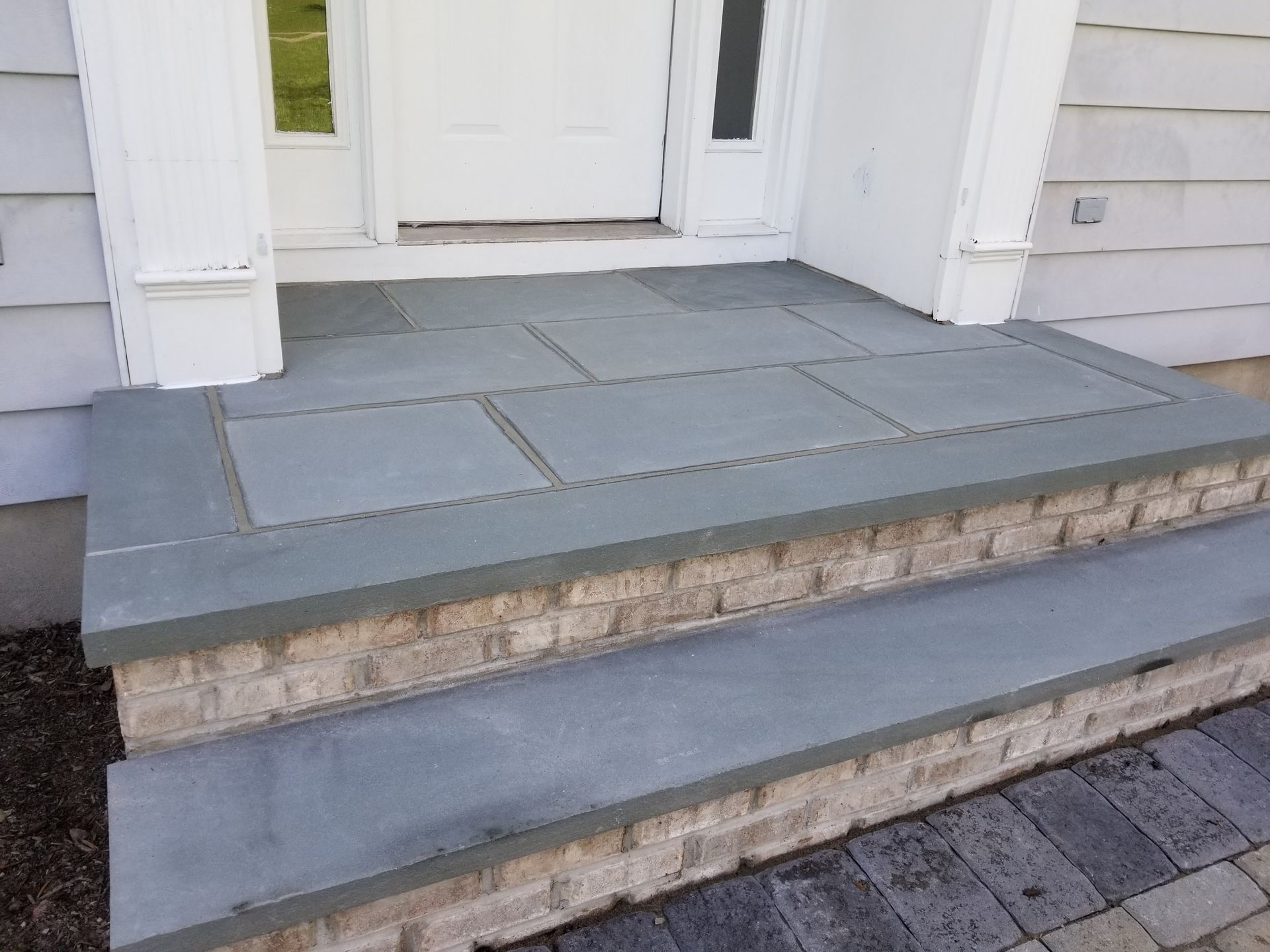 Front porch steps with gray stone pavers leading to a white front door