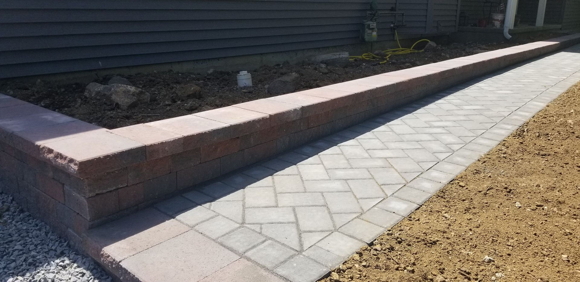 Brick retaining wall beside a light gray paver walkway in a landscaped yard