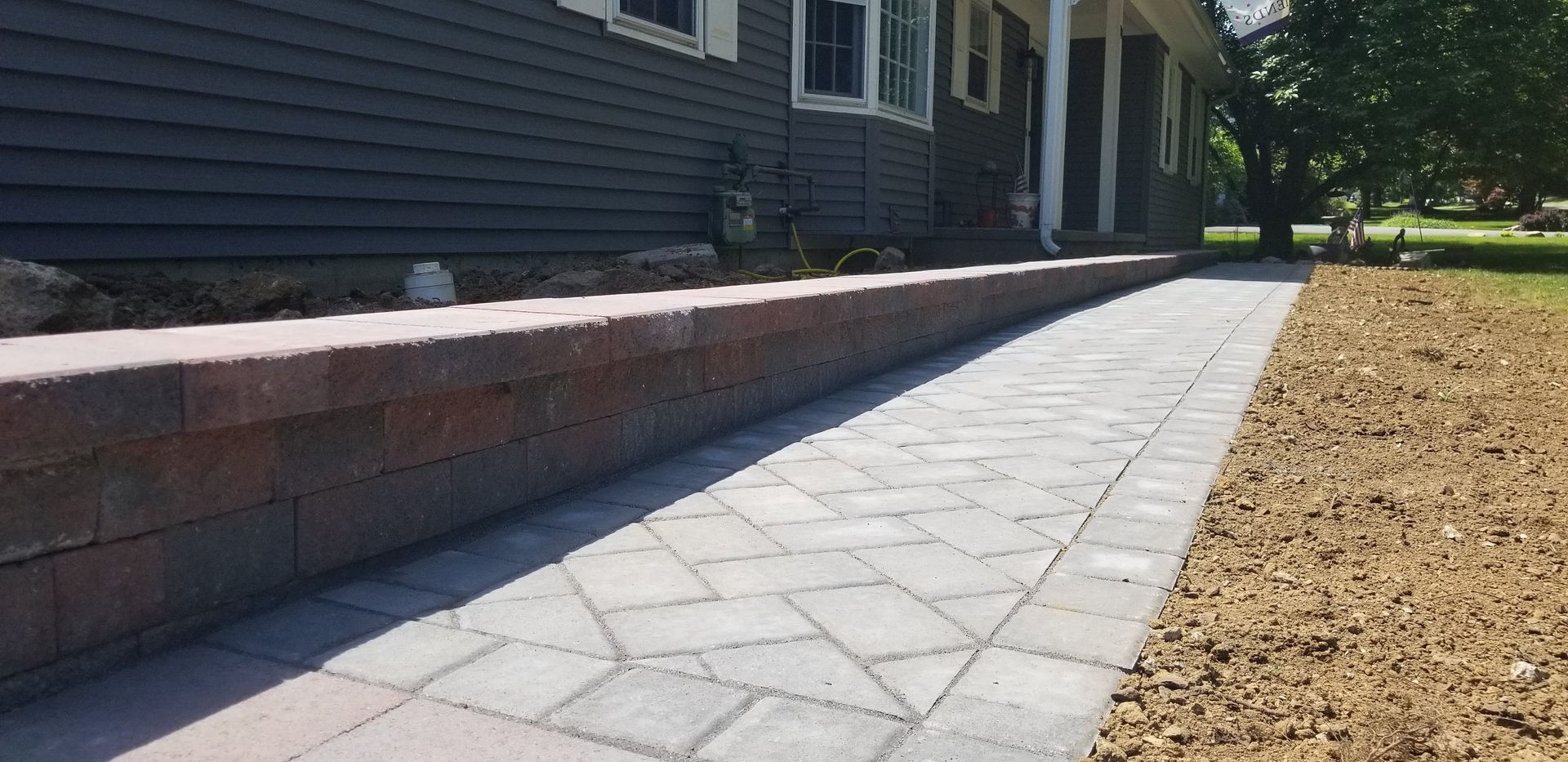 Stone walkway beside a house and brick retaining wall, with dry grass on the right