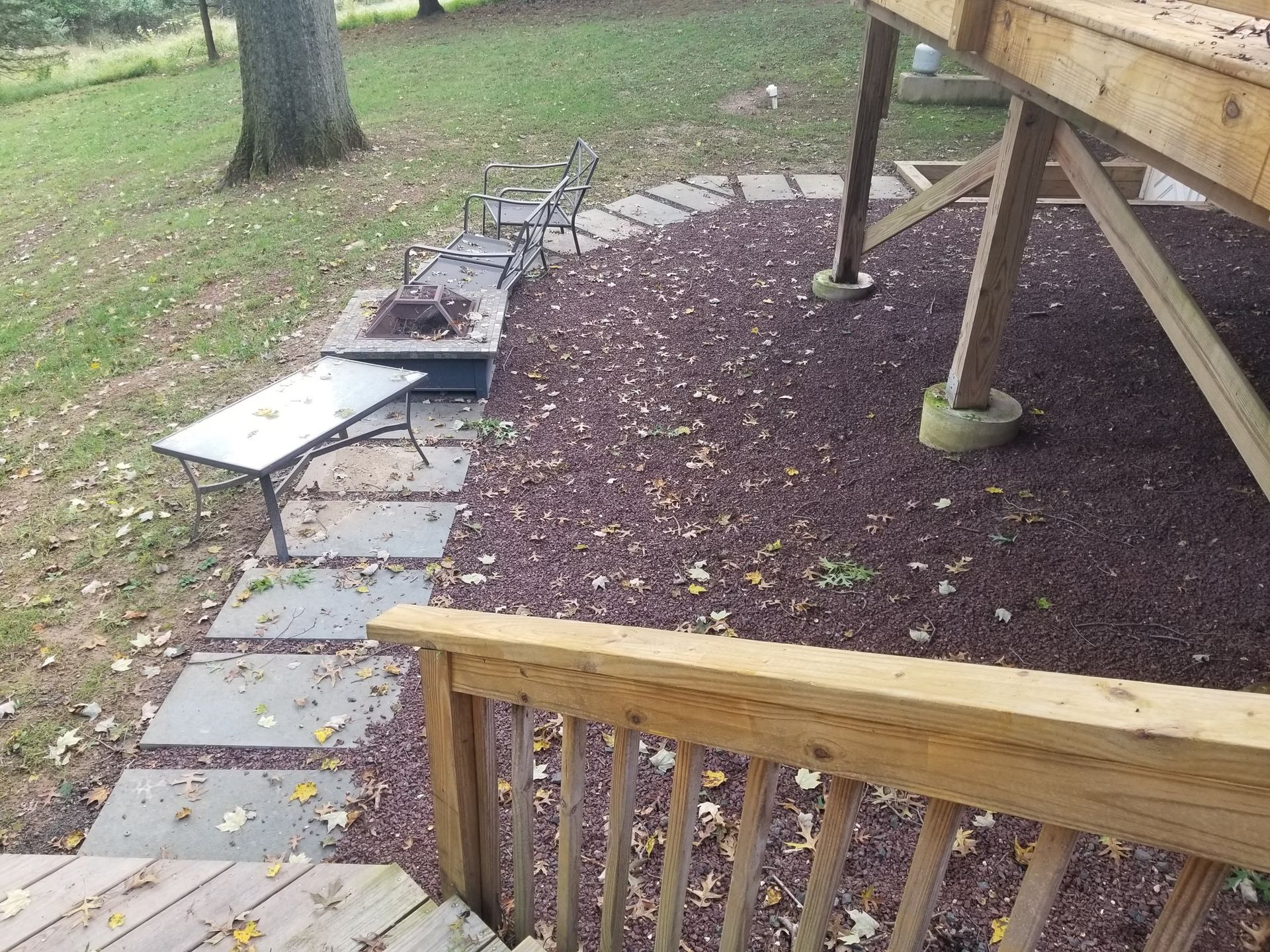 Backyard deck with wooden railing, stone path, and fire pit area under a raised patio