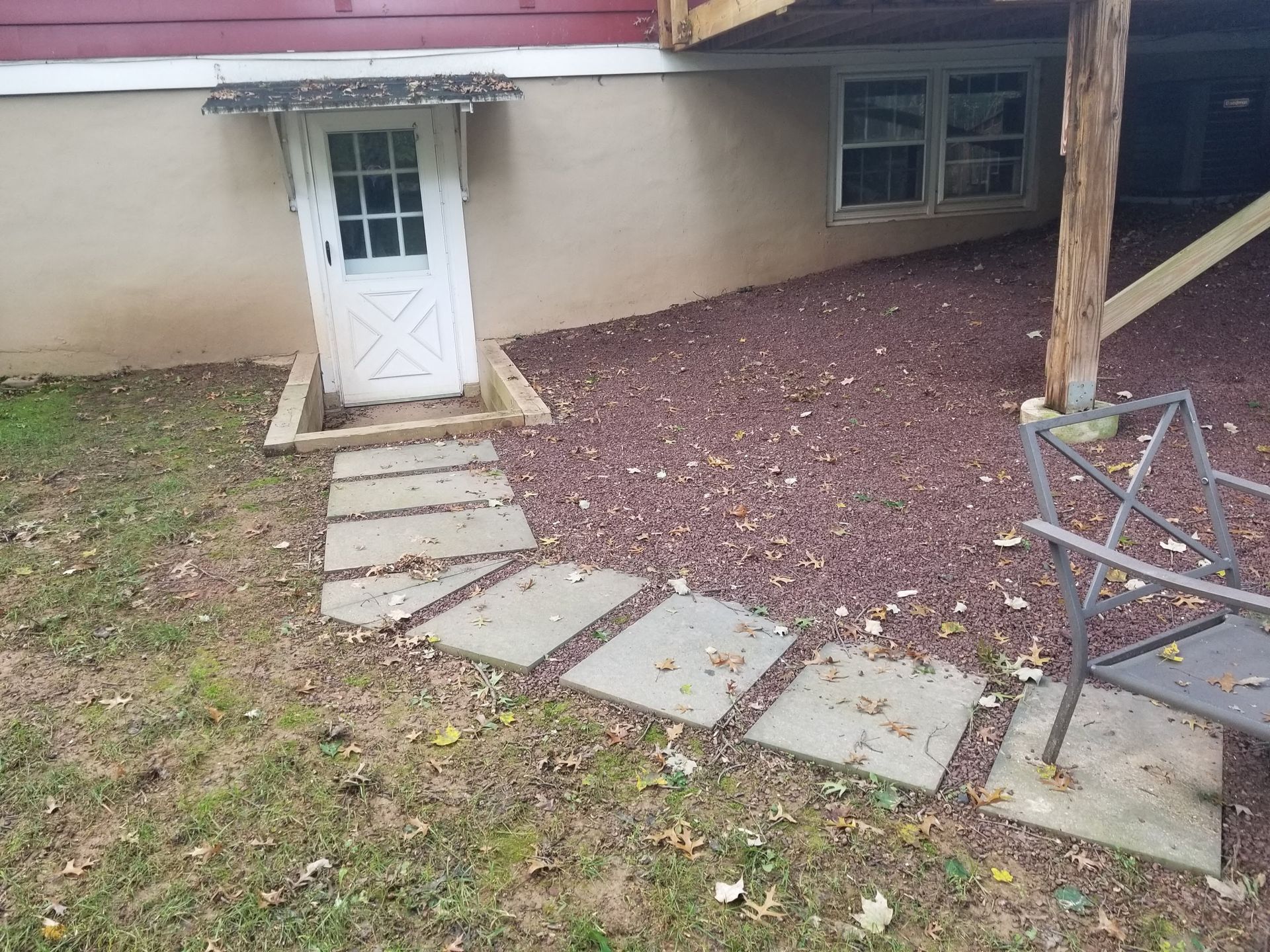 Backyard walkway with stepping stones, white door, and a star-shaped metal chair under a house overhang