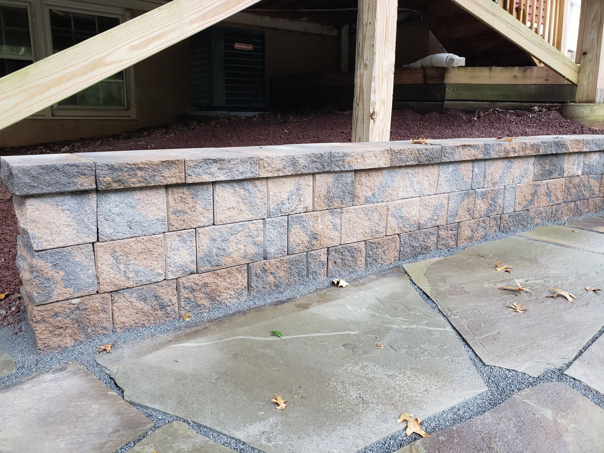Stone retaining wall beneath wooden deck with cracked concrete sidewalk in front