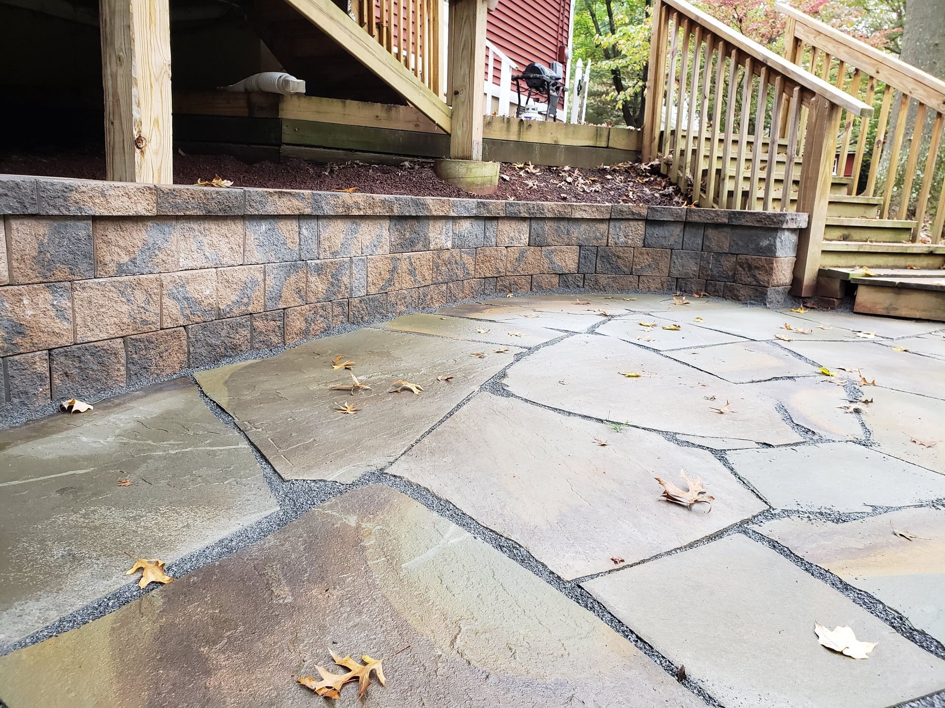 Wet stone patio beside a brick retaining wall and wooden stairs with railings