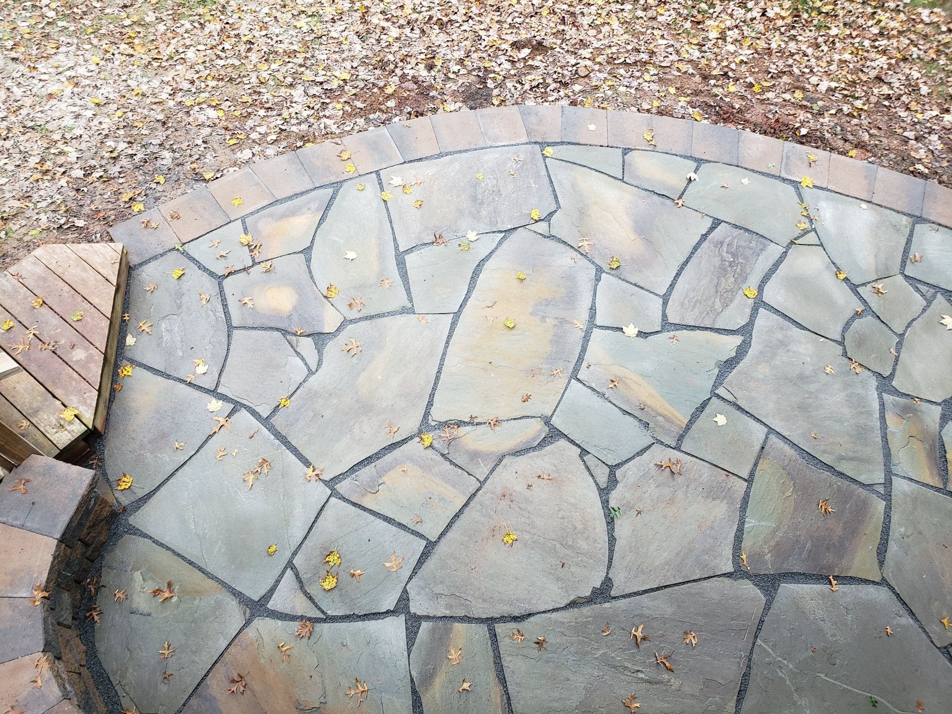Stone patio with irregular gray pavers, bordered by gravel and a small brick step.