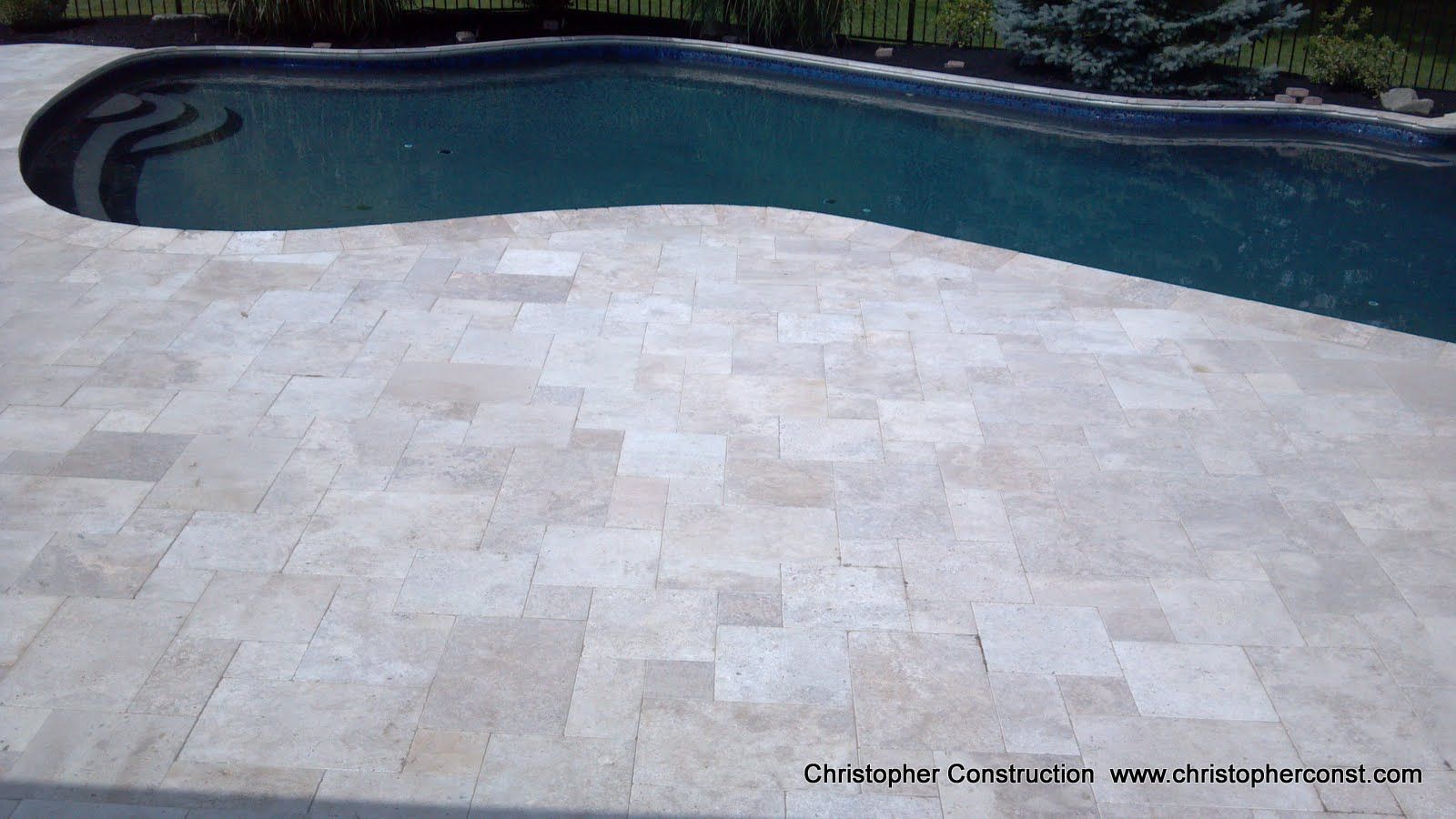Stone patio beside a dark blue swimming pool with a curved edge
