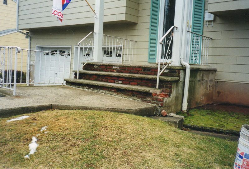 Front steps of a house with railings, concrete walkway, and wet lawn after rain