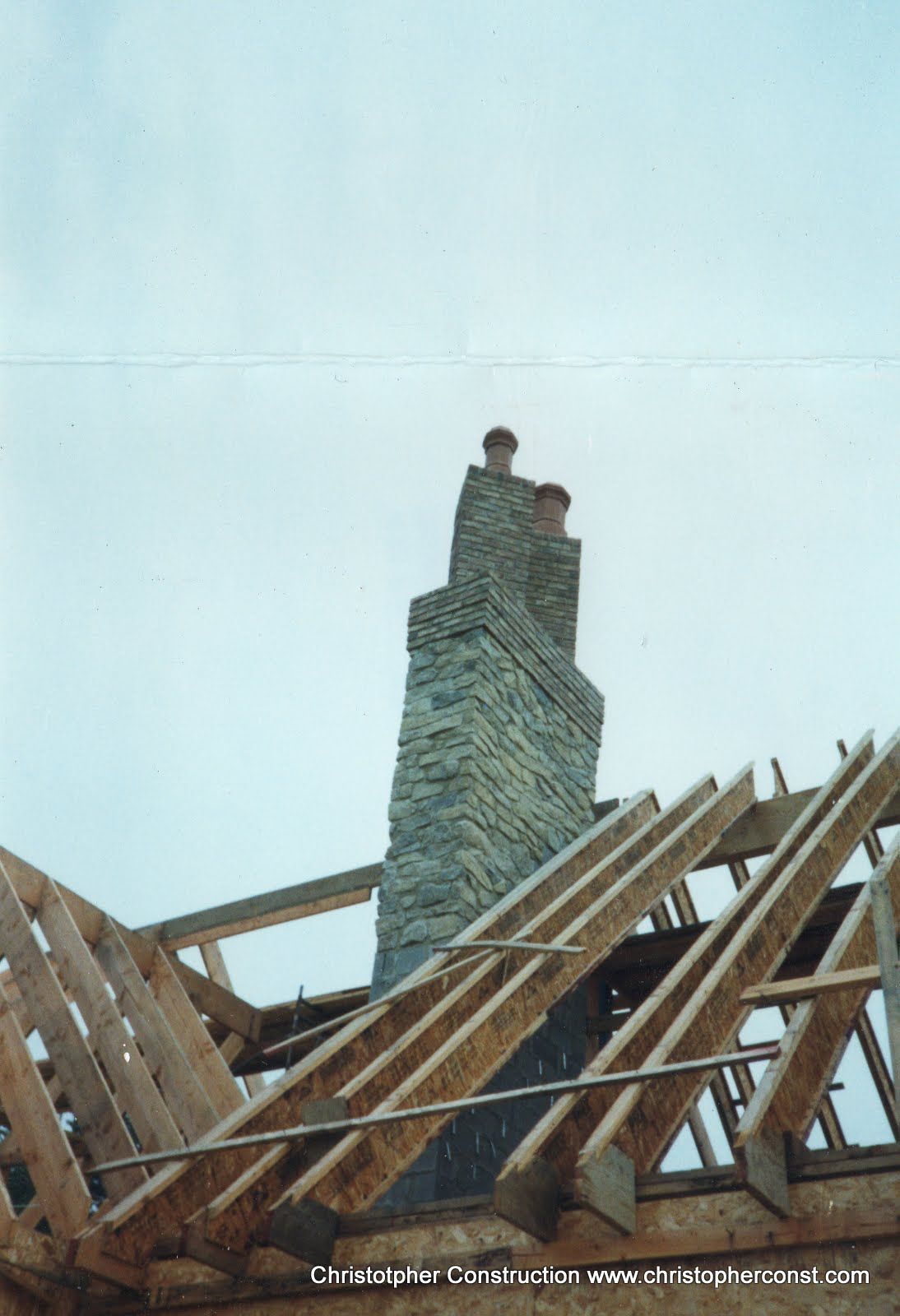 Roof framing around a tall stone chimney against a pale sky