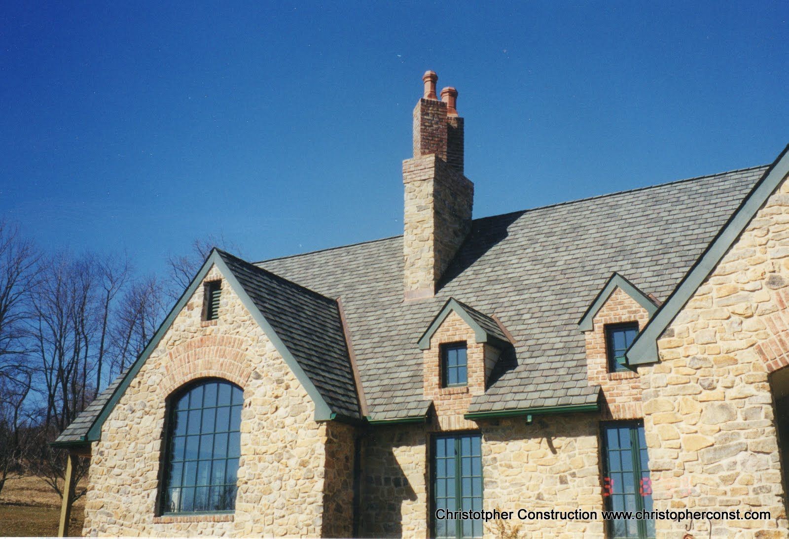 Stone house with steep gray roof and tall chimney under a clear blue sky