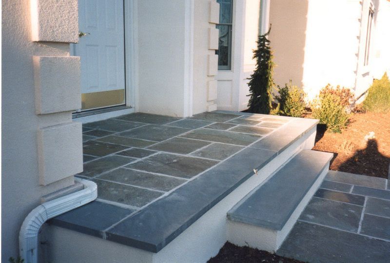 Front steps and tiled porch entrance of a white house with a short staircase and walkway