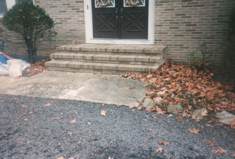 Front steps of a brick house with cracked concrete and a pile of fallen leaves on the right