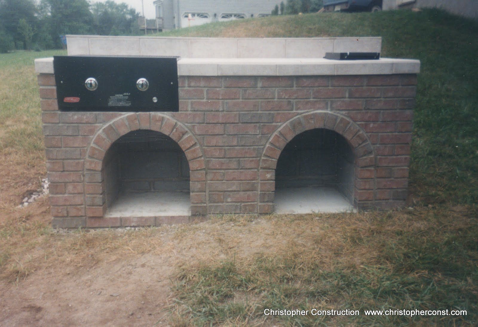 Brick outdoor fireplace with two arched openings and a black control panel on the left