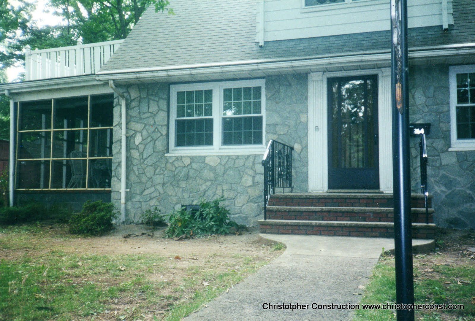 Stone house front entrance with blue door, steps, porch, and windowed screened area