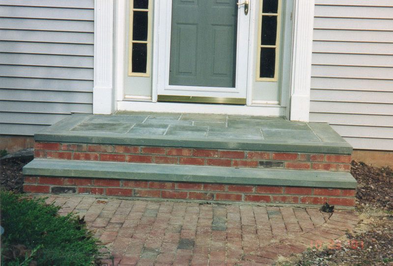 Brick front steps leading to a house entrance with a white-framed door and gray siding