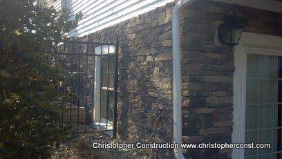 Stone-clad house exterior with a white-trimmed window, black wall lantern, and a small garden gate