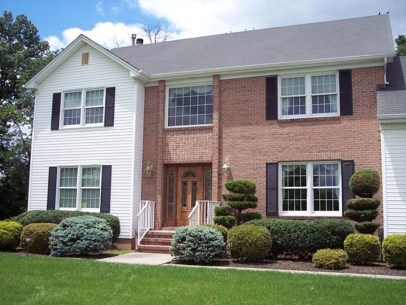Suburban two-story brick and white house with manicured shrubs and a front lawn