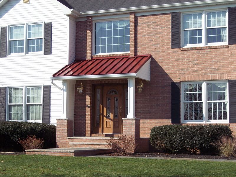 Brick townhouse entrance with red awning, white siding, and trimmed shrubs