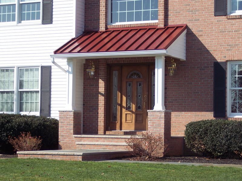 Brick apartment entrance with red metal awning, white columns, and wooden front door
