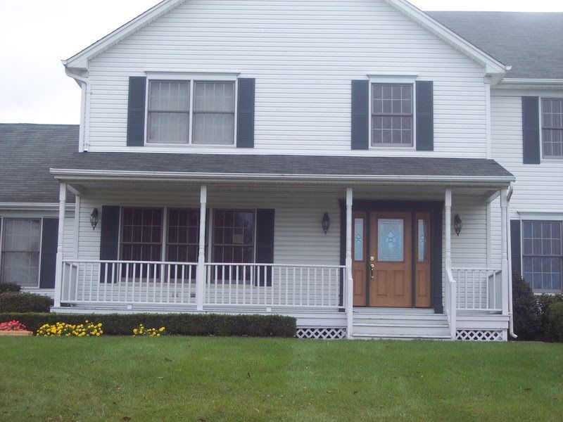 White two-story house with a covered front porch, dark shutters, and double wooden front doors