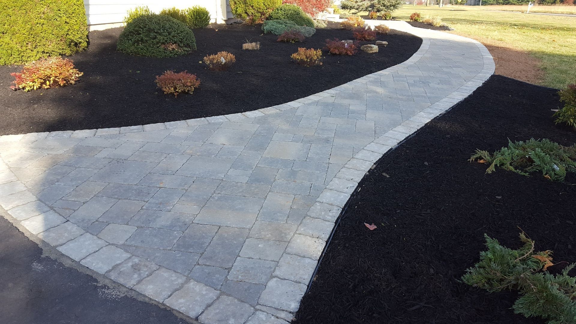 Curved light stone garden path bordered by dark mulch and small shrubs