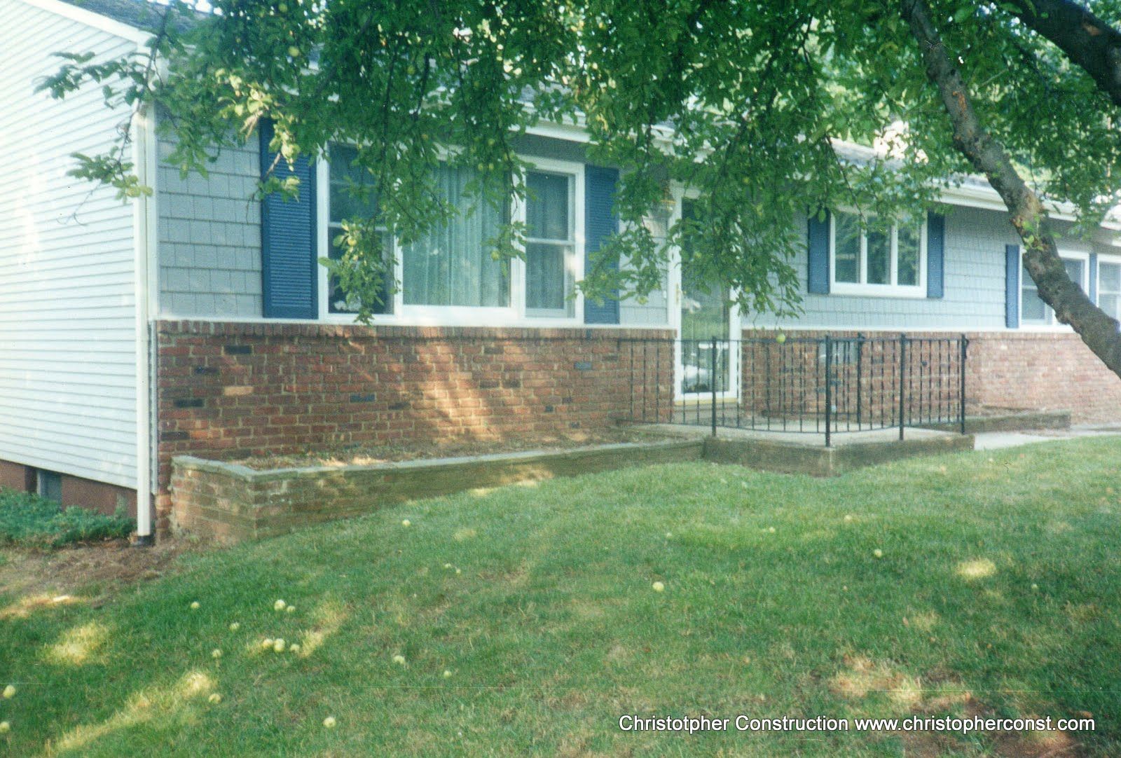 Brick house with blue shutters, front lawn, and a porch under leafy trees