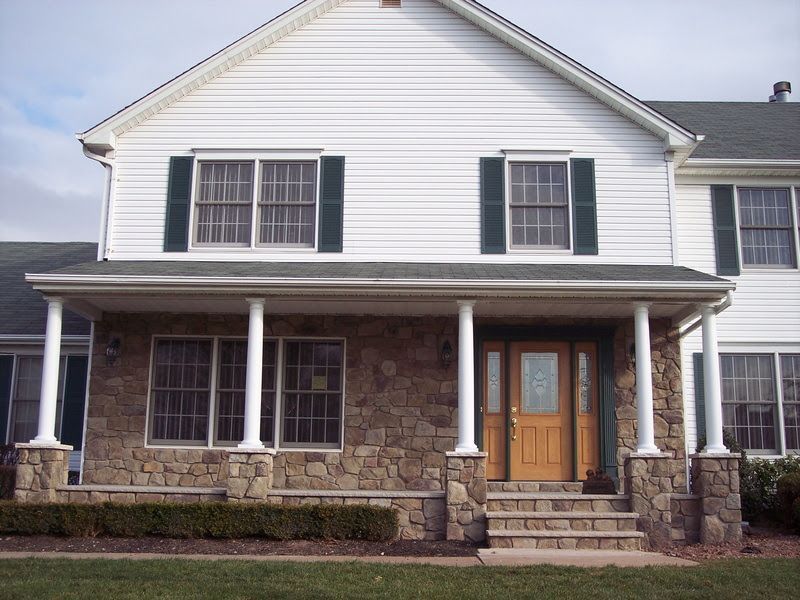 Two-story white house with stone porch, black shutters, and front steps
