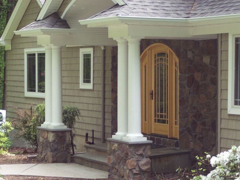 Front porch with white columns, stone base, and a yellow front door on a house exterior.