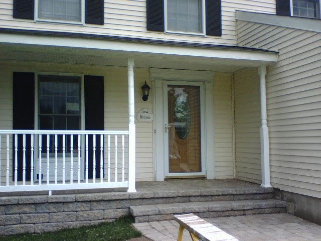 Front porch with white railing, beige siding, steps, and a glass storm door on a house