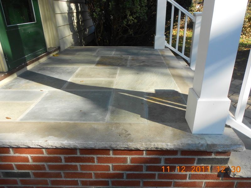 Concrete front porch with white railing and red brick foundation in sunlight