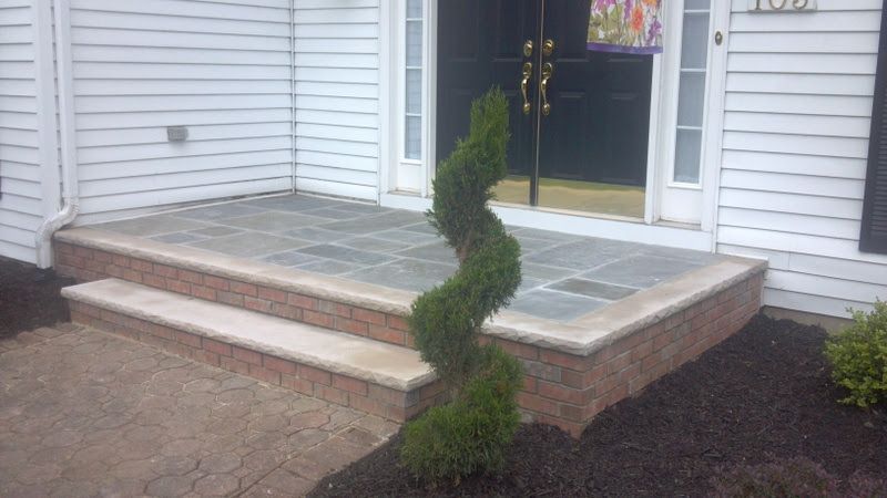 Front porch with gray stone steps and a small spiral evergreen beside a white house entrance.